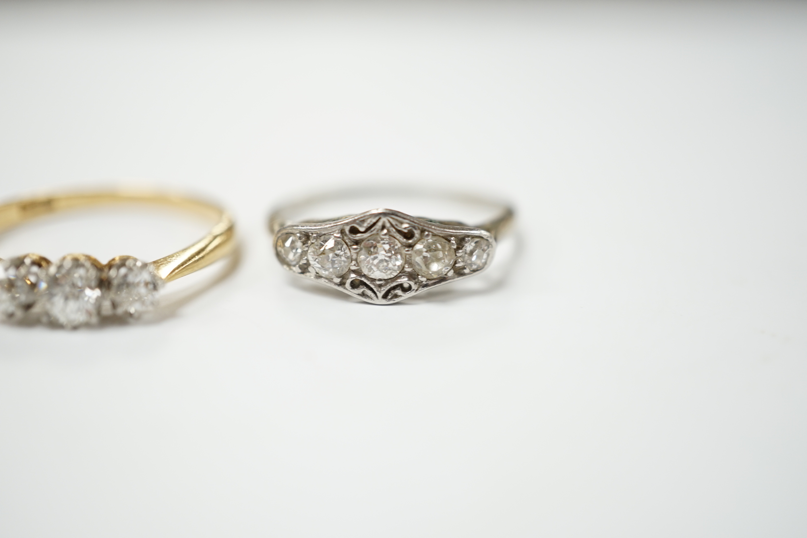 An 18ct gold three stone diamond ring, size M and a white metal five stone diamond dress ring, size M